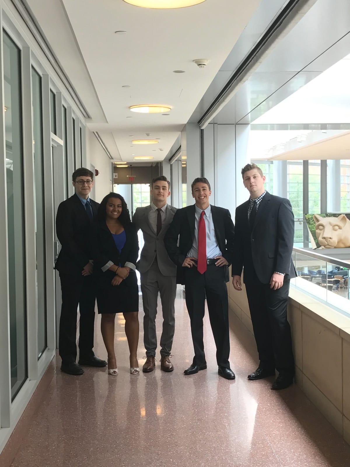 Five members of the PSU Trading Society executive board standing in an upper-floor hallway overlooking the Business Building atrium