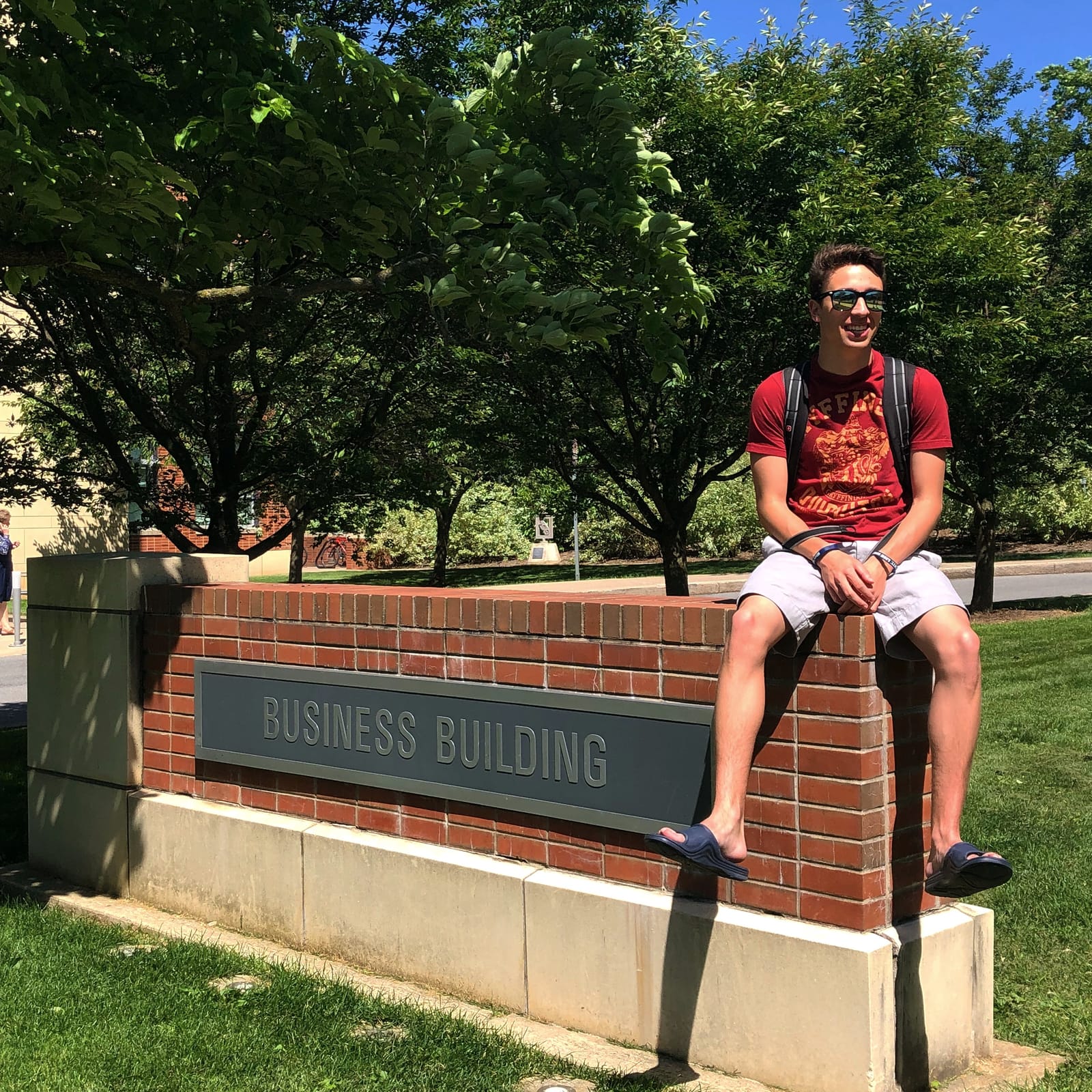 Christopher R. Peckyno seated on the Business Building sign at Penn State on a summer day