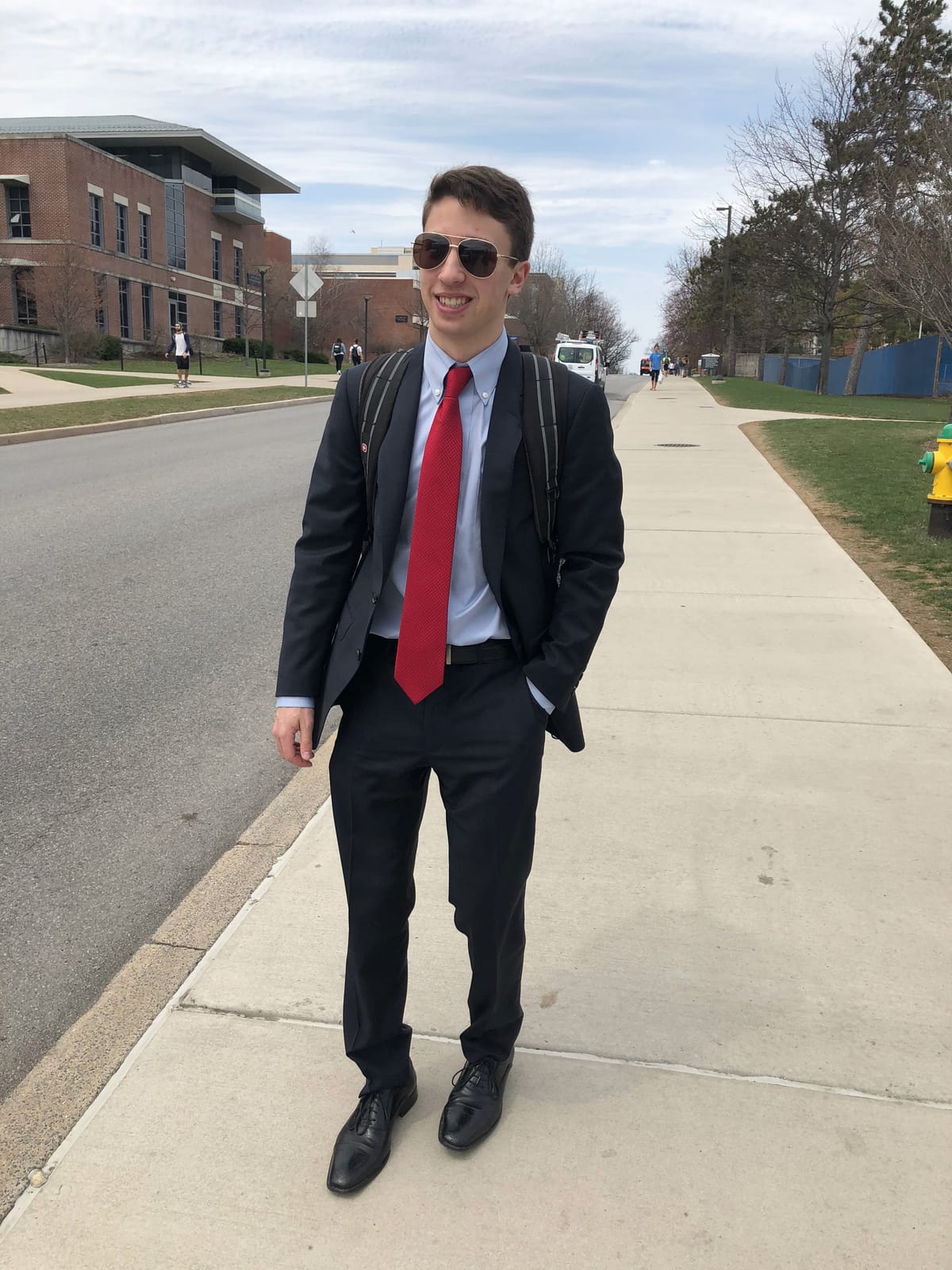 Christopher R. Peckyno in a navy suit and red tie walking along a campus sidewalk at Penn State
