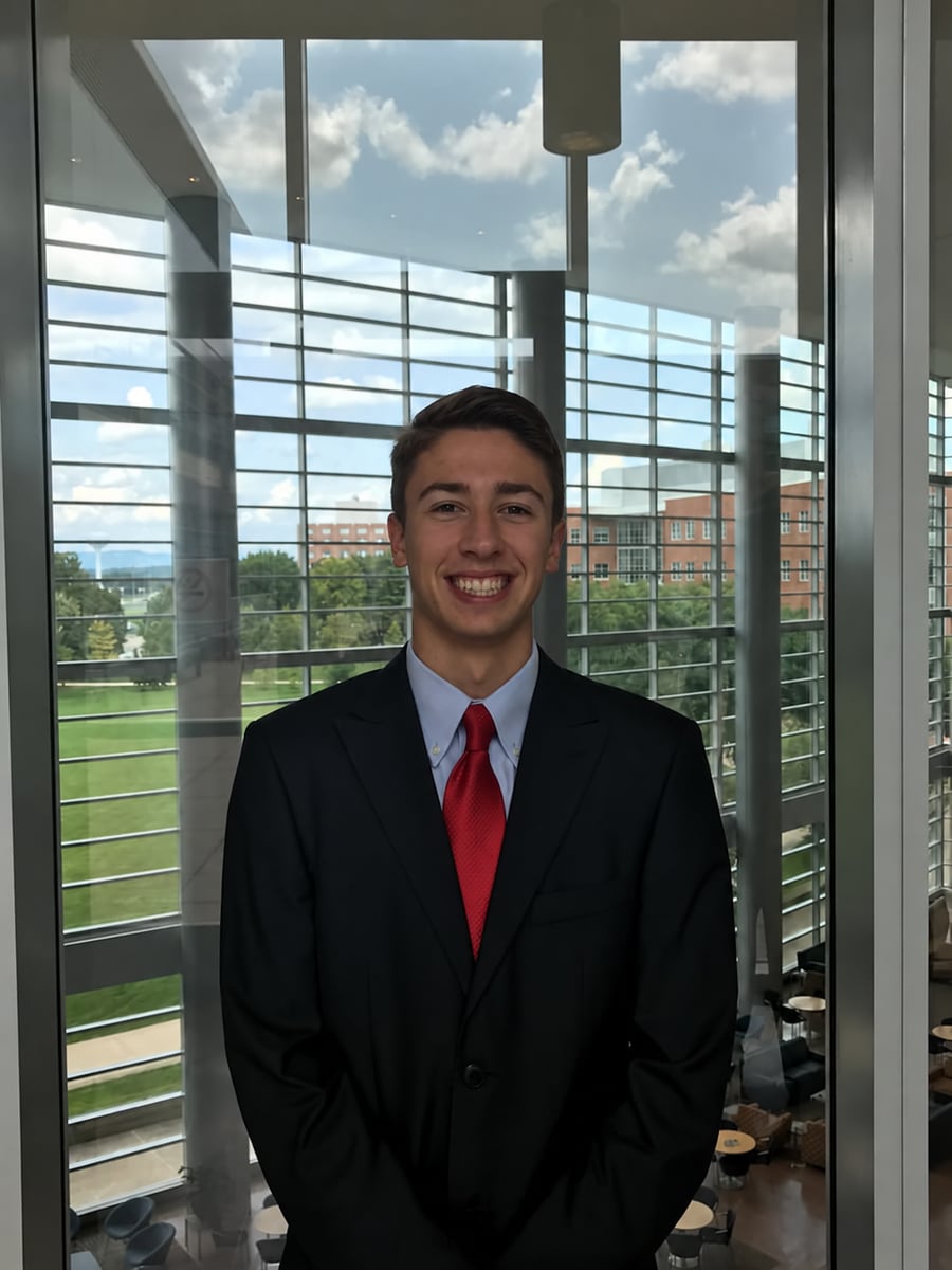 Christopher R. Peckyno, founder of the PSU Trading Society, in a dark suit and red tie in front of the atrium windows of the Business Building at Penn State